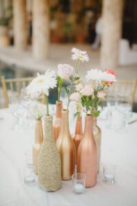 DIY painted rose gold painted wine bottles with flowers inside on table.