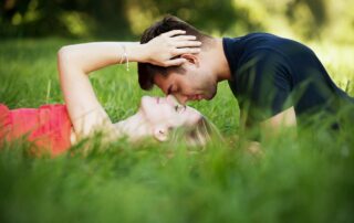 Couple laying in grass with the man kissing the woman's forehead.