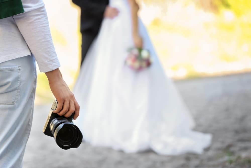 Professional,Photographer,With,Camera,And,Wedding,Couple,,Outdoors